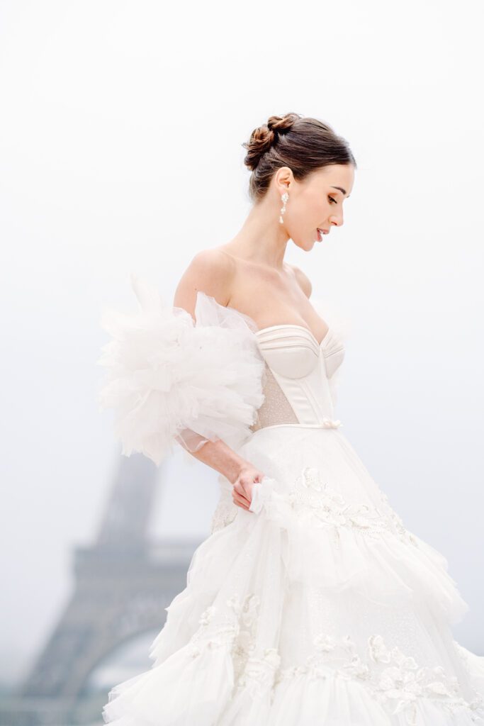 Paris pre-wedding session in front of the Eiffel Tower while it is covered in fog with bride in full train layered gown with separate off the shoulder full puffed sleeves and groom in a navy blue suit photographed by Italy destination photographer